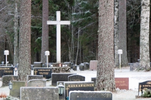 Hautausmaalla näkyy hautakivien takaa suuri, valkoinen risti